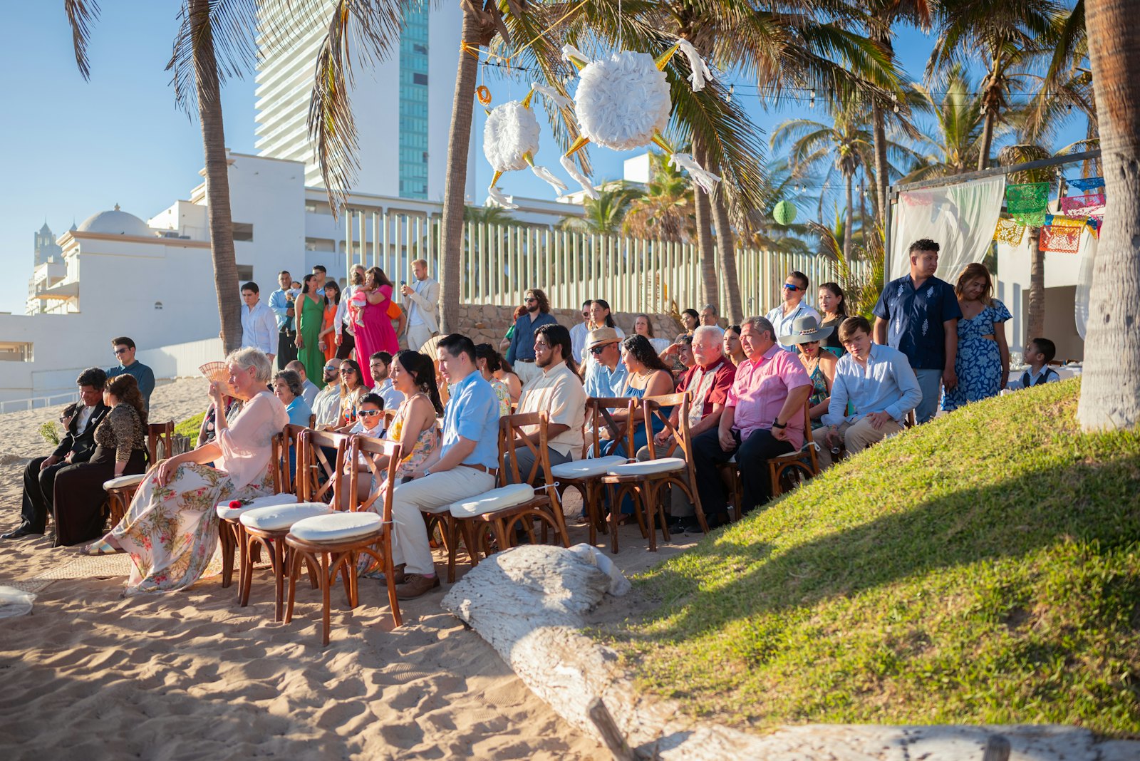 About forty guests seated on a beach for a destination wedding, under palm trees.